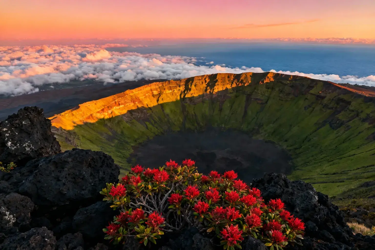 Crête du volcan Haleakala à Maui avec ciel orange et rose, mer de nuages et pentes vertes contrastant avec les roches volcaniques noires