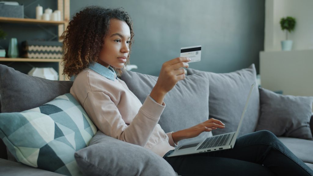 femme utilisant un ordinateur portable et une carte de crédit sur un canapé
